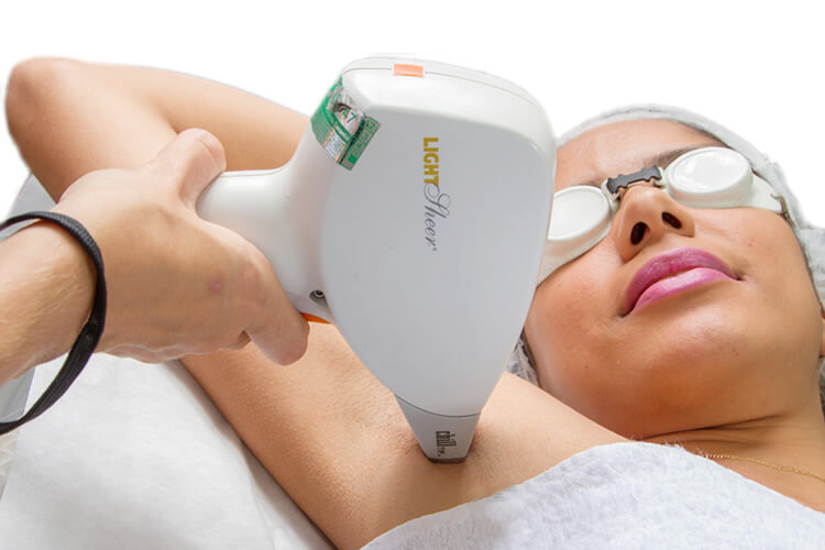 A imagem mostra uma pessoa recebendo um tratamento de depilação a laser na região das axilas. O dispositivo utilizado é o "Light Sheer", segurado por uma mão com uma pulseira preta. O paciente está deitado sobre uma superfície branca, possivelmente uma maca clínica ou de spa, com uma toalha cobrindo parte do corpo. O procedimento é comum para reduzir ou eliminar o crescimento de pelos em áreas específicas.