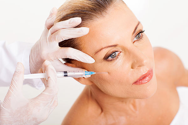 A imagem mostra um procedimento estético onde uma pessoa recebe uma injeção de Botox na região da testa. O profissional que administra a injeção está usando luvas brancas, garantindo um ambiente estéril. O procedimento é amplamente utilizado para suavizar rugas e linhas de expressão, proporcionando um aspecto mais rejuvenescido.