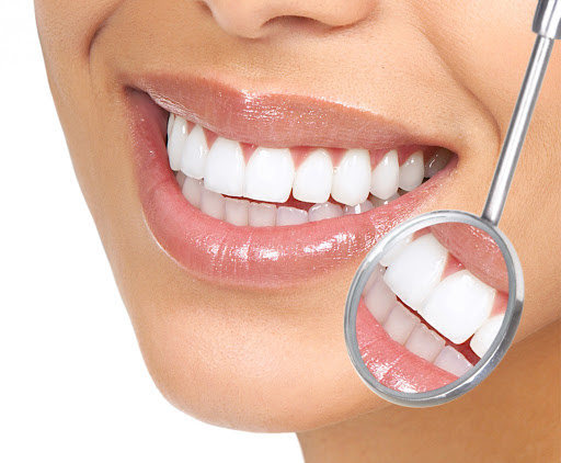 A imagem mostra um close-up da boca de uma pessoa sorrindo, destacando dentes brancos e bem alinhados. Um espelho odontológico reflete parte dos dentes, enfatizando sua limpeza e saúde. A composição ressalta a importância dos cuidados dentários para manter um sorriso saudável e bonito.